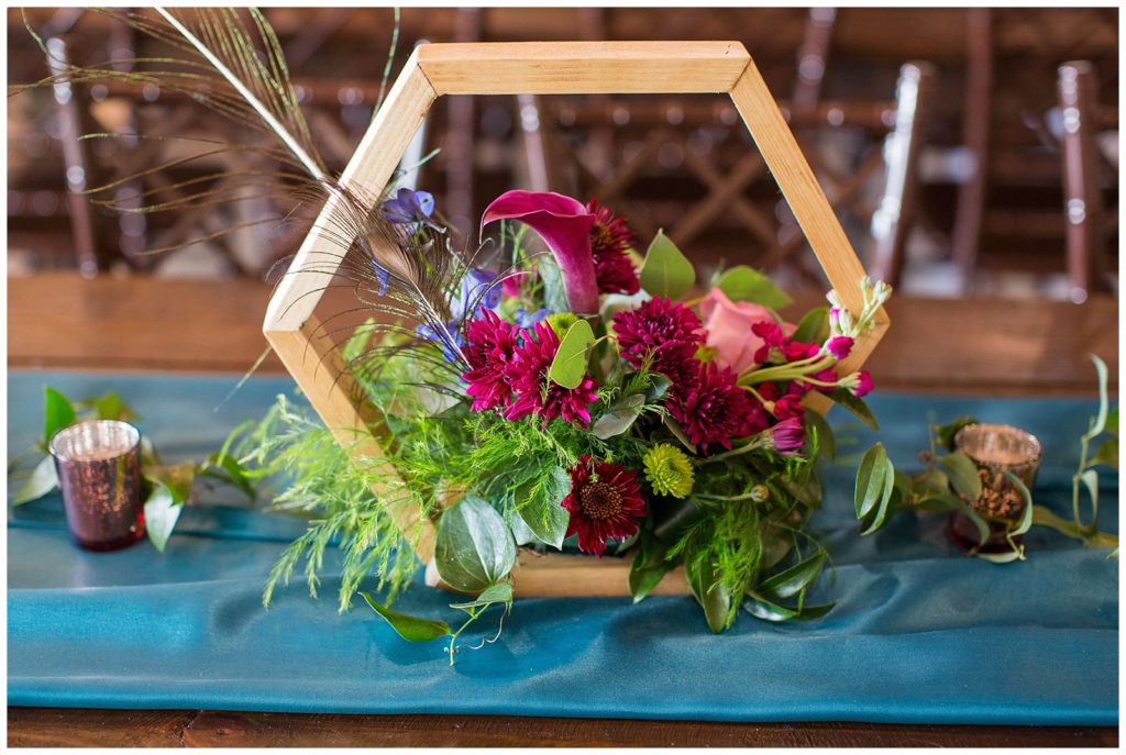 Jewel toned colors in wood hexagon centerpiece | Peacock themed wedding at Emery's Buffalo Creek 